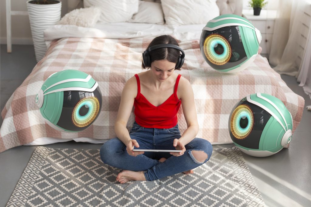 Photo d'une femme assise au pied d'un lit, avec des écouteurs sur les oreilles. 3 grosses cameras en forme d'oeil sont autour d'elle